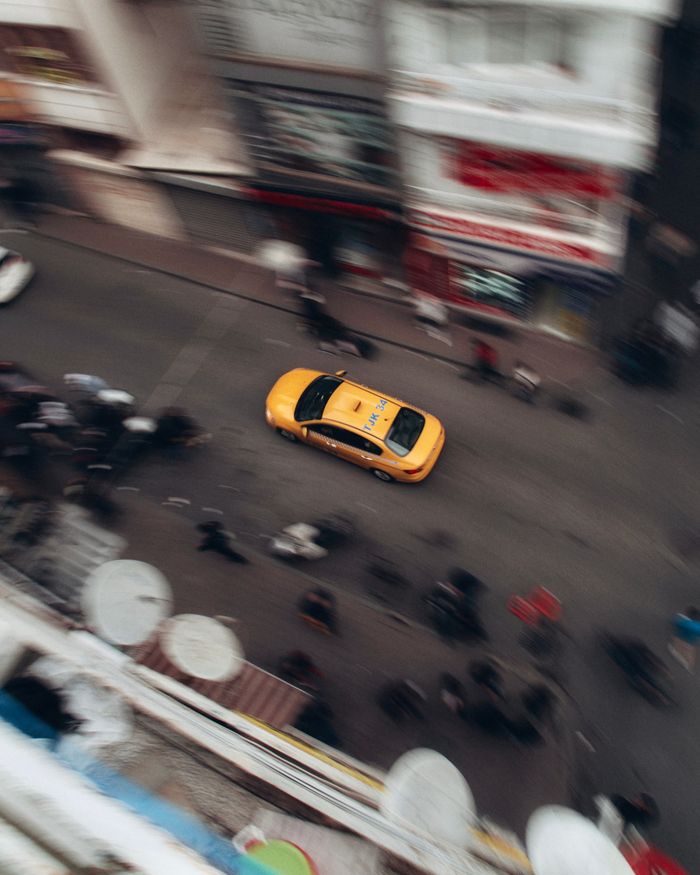 contact-img Aerial view of a vibrant city street with a yellow taxi moving swiftly among blurred pedestrians.