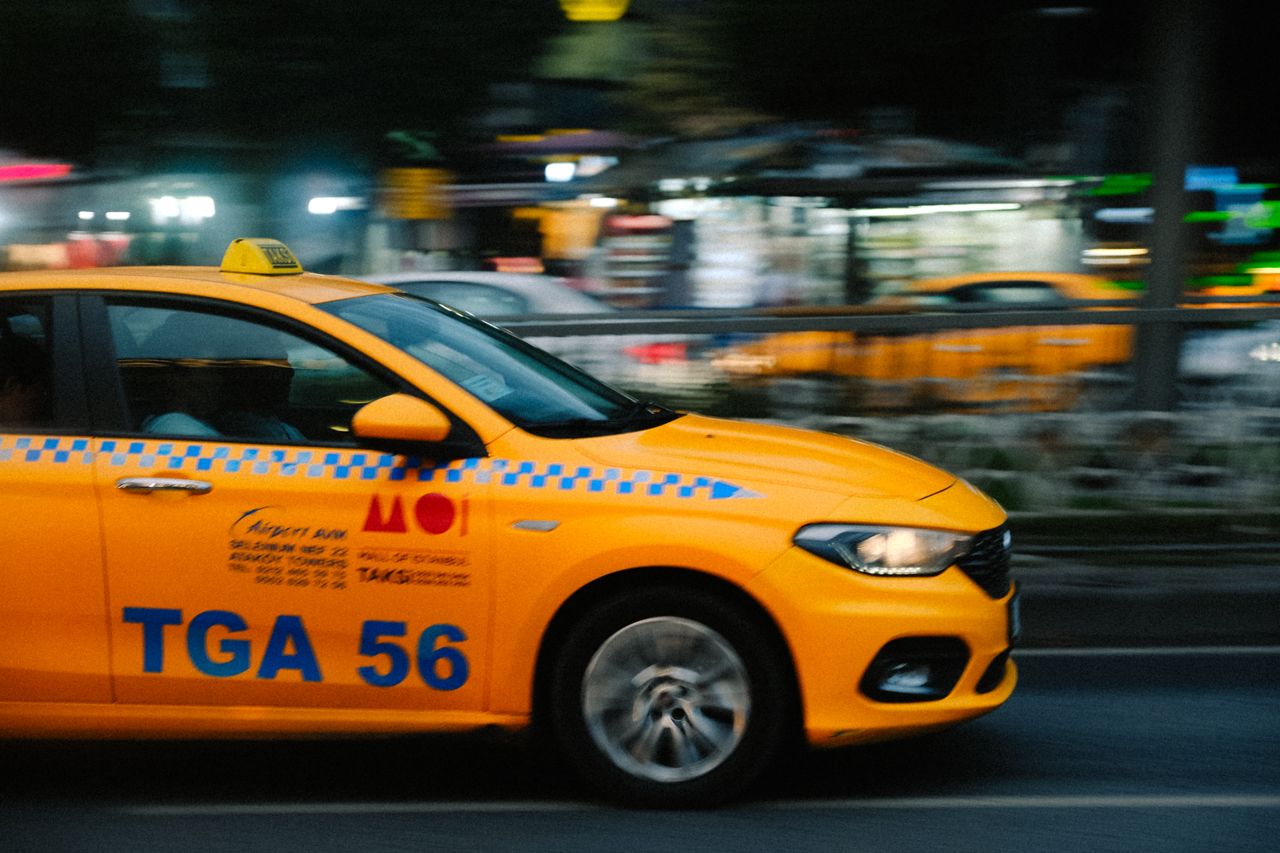 gallery-1 Dynamic shot of a yellow taxi speeding through city streets at night, capturing urban life.
