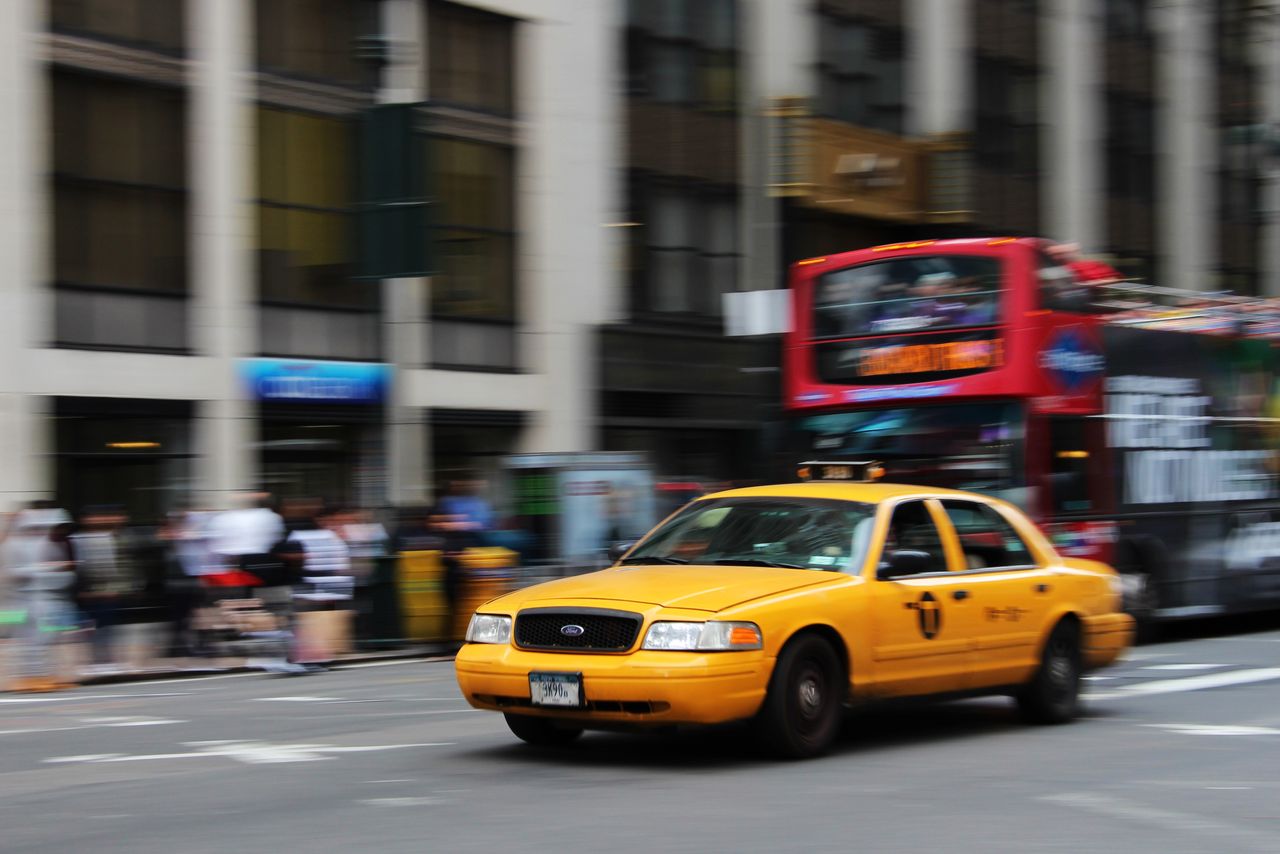 our-experience A yellow taxi speeds through the vibrant streets of New York City, capturing urban life and motion.