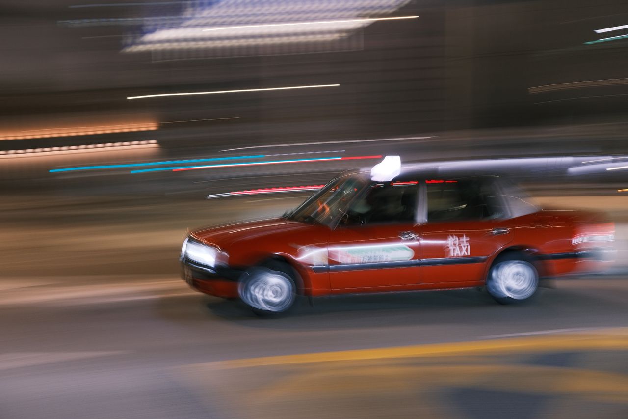 services-02 A red taxi captured in motion blur racing through the city streets at night.