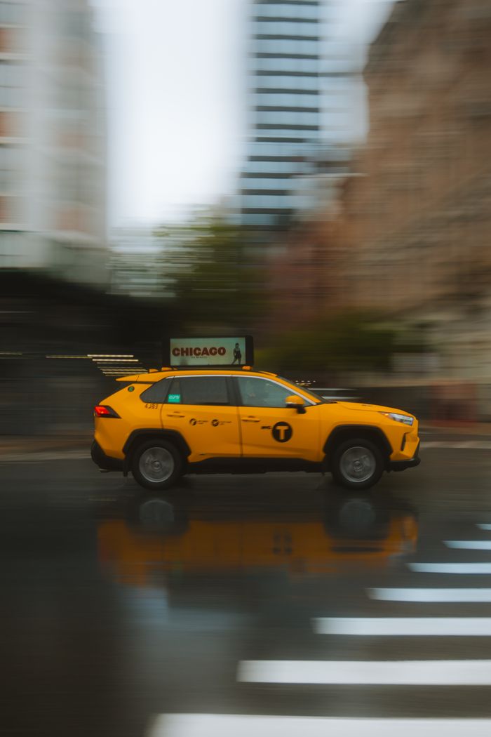 services-03 A yellow taxi drives through the city streets on a rainy day, captured in motion blur.