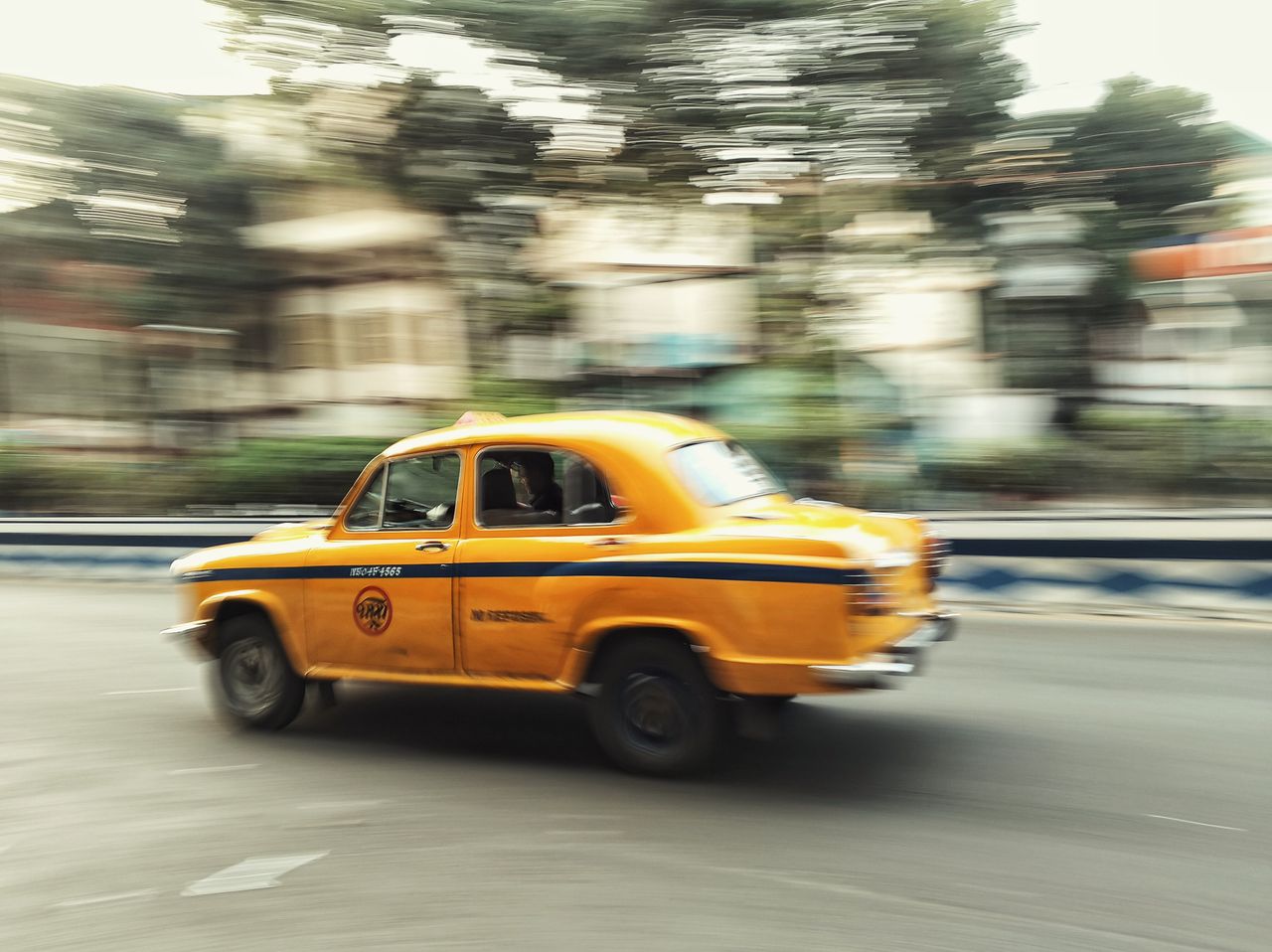 about-img A vintage yellow taxi speeds along a city street, blending motion blur with urban life.