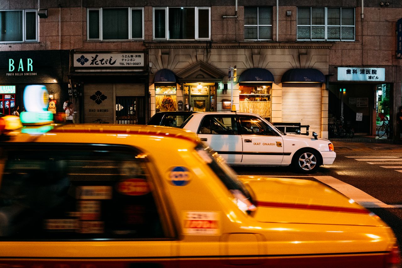 services-04 Dynamic Tokyo street scene featuring yellow taxis and illuminated storefronts at night.