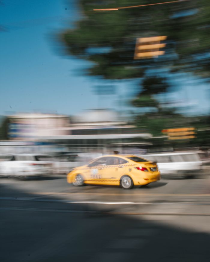 gallery-5 Yellow taxi in motion captured with blur effect on a busy urban street.